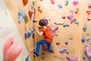 Boy climbing on artificial boulders wall in gym