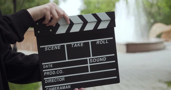Unrecognizable man claps with clapperboard and leaves the video frame.