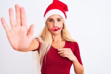 Woman wearing Christmas Santa hat holding fanny mustache over isolated white background with open hand doing stop sign with serious and confident expression, defense gesture