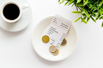 Pay restaurant bill by cash. Reciept and coins on plate on white background top view