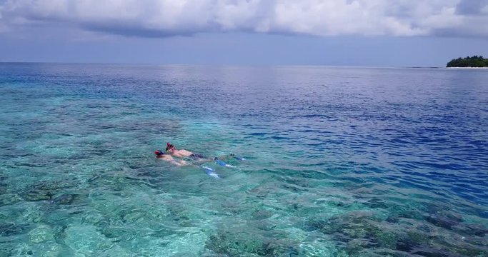 Young couple snorkel over clear water of shallow lagoon watching corals over white sand of seabed and tropical fish in Maldives