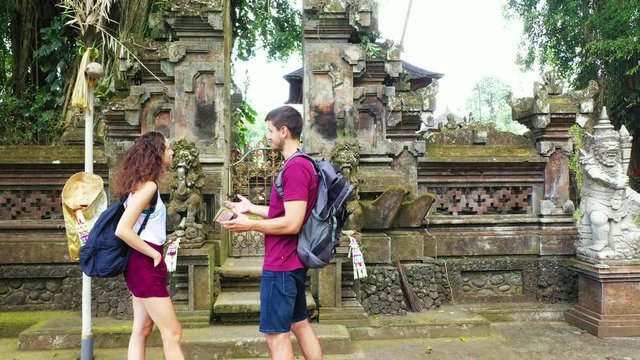 Young couple discussing in front of the temple, guy with a tourist map on hand waiting to open the temple's door in Bali