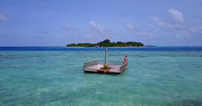 Lonely girl relaxing on floating platform over clear crystal water of shallow lagoon near tropical island shore in Barbados