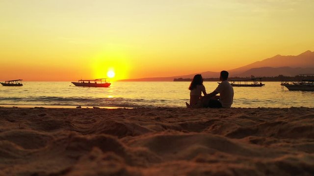 Couple in love enjoying romantic sunset with yellow sun over gloaming orange horizon through silhouette of long boats on calm lagoon in Philippines