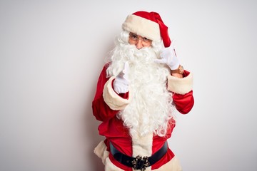 Middle age handsome man wearing Santa costume standing over isolated white background smiling doing talking on the telephone gesture and pointing to you. Call me.