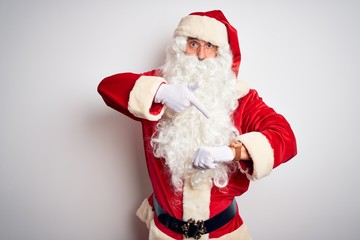 Middle age handsome man wearing Santa costume standing over isolated white background In hurry pointing to watch time, impatience, upset and angry for deadline delay