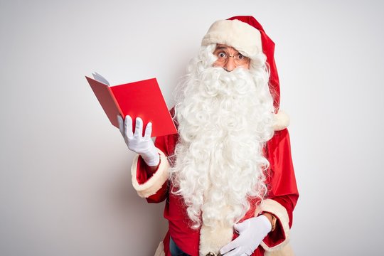 Middle age man wearing Santa Claus costume reading book over isolated white background puffing cheeks with funny face. Mouth inflated with air, crazy expression.