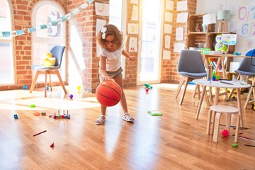 Beautiful toddler playing with basketball ball around lots of toys smiling at kindergarten