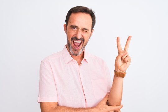 Middle age handsome man wearing casual pink shirt standing over isolated white background smiling with happy face winking at the camera doing victory sign. Number two.
