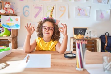 Beautiful toddler wearing glasses and unicorn diadem sitting on desk at kindergarten relax and...