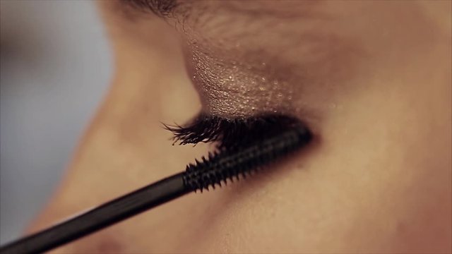 Female eye close-up. Brown and gold shadows, black mascara in makeup. Applying makeup. Promotional concept of false eyelashes, lenses, vision correction, mascara, eye shadow
