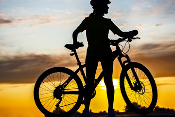 Fototapeta na wymiar Silhouette of a girl cyclist with a bicycle on the background of a sunset sky.