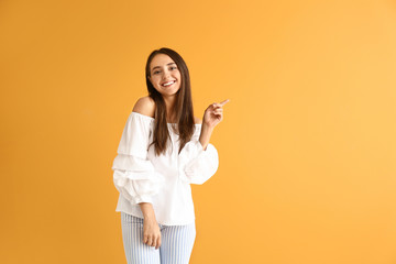 Beautiful young woman showing something on color background