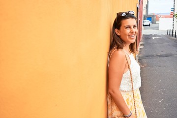 Obraz na płótnie Canvas Beautiful girl leaning on orange wall, young friendly woman smiling happy on a sunny day of summer