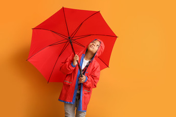 Fashionable African-American boy in autumn clothes and with umbrella on color background