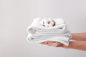 Female hands with beautiful cotton flowers and soft towels on grey background
