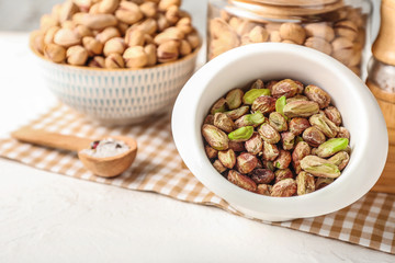 Bowl with tasty pistachio nuts on table