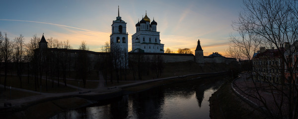 Panorama of the ancient medieval fortress and houses standing on the banks of the river. The city landscape is illuminated by the soft rays of the setting sun. Pskov, Russia.