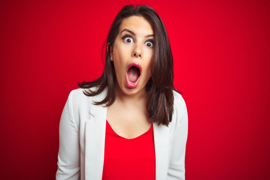 Young beautiful business woman wearing elegant jacket over red isolated background afraid and shocked with surprise expression, fear and excited face.