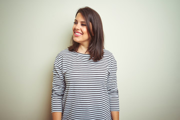Fototapeta premium Young beautiful brunette woman wearing striped sweater over white isolated background looking away to side with smile on face, natural expression. Laughing confident.