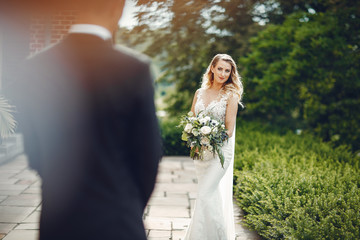 Beautiful bride in a long white dress. Handsome groom in a black suit. Couple in a summer park
