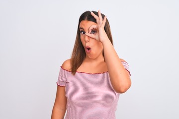 Portrait of beautiful young woman standing over isolated white background doing ok gesture shocked with surprised face, eye looking through fingers. Unbelieving expression.