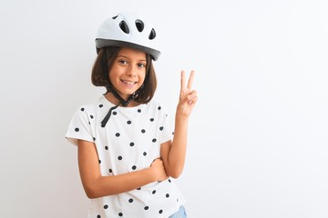 Beautiful child girl wearing security bike helmet standing over isolated white background smiling with happy face winking at the camera doing victory sign. Number two.