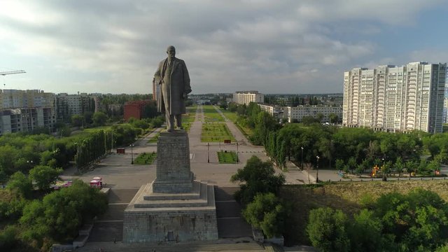 Drone forward close up concrete monument leader Lenin socialist communist landmark typical central square Russia. Historical cityscape. Soviet and modern houses. Summer clouds open space skyline