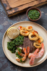 Round beige plate with surf and turf meal, vertical shot over brown stone background, elevated view