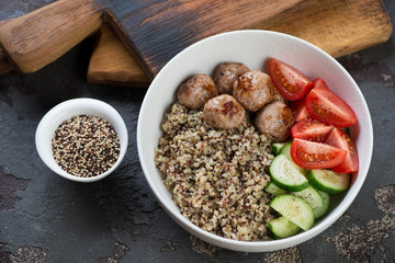 Food bowl with quinoa, fried meatballs and fresh vegetables, studio shot over brown stone background