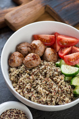Close-up of quinoa, roasted meatballs and vegetables served in a white bowl, vertical shot