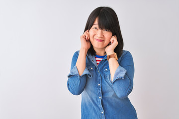 Young beautiful chinese woman wearing denim shirt over isolated white background covering ears with fingers with annoyed expression for the noise of loud music. Deaf concept.