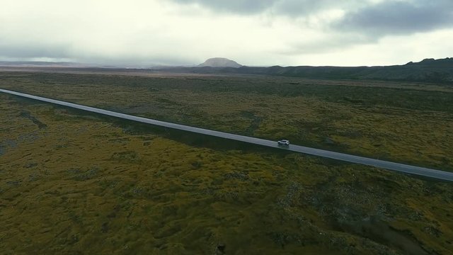 4WD off-road jeep with turned on headlights is driving up the green hill by the unpaved dirt gravel road. The cloudy sky and blue sea on the background at the dusk. Sprengisandur, Iceland. oktober