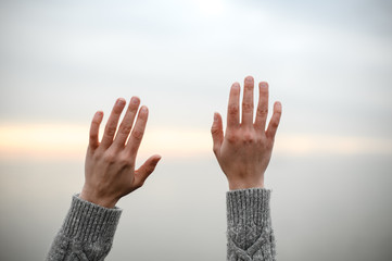 beautiful young hands in a warm woolen sweater raised up to the sky on a sunset background - 303759745