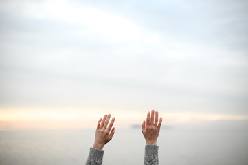 beautiful young hands in a warm woolen sweater raised up to the sky on a sunset background