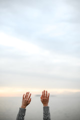 beautiful young hands in a warm woolen sweater raised up to the sky on a sunset background - 303759762