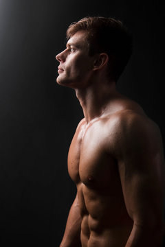 Muscular bodybuilder posing with a naked torso on a black background in the dark with backlight. Sexy man.
