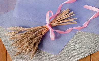 Beautiful delicate bouquet with pink ribbon of dried  wheat ears on the table with a purple sheet...