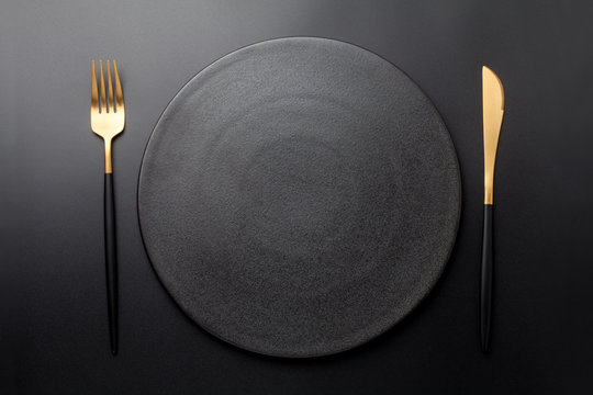 Empty black plate with fork and knife on black background. Top view.