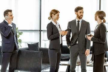 White-collar employees of financial institution or other big copany having some business, standing and talking in the luxury office