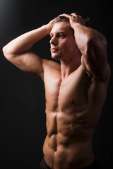 Bodybuilder holds muscular arms on head. Photo in studio on a black background.