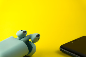 Bluewireless bluetooth earphones or headphones, plastic case or box for storage and charging and smartphone on black background, close up