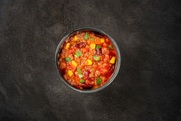 Chili con carne, a Mexican stew with beans, ground meat, corn, and chilli peppers, shot from the top on a dark background