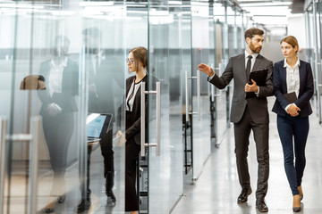 Business people walking in the hallway of the modern office building with employees working behind glass partitions. Work in a large business corporation