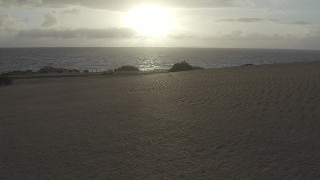Low desert aerial over sand towards coastal road at sunrise