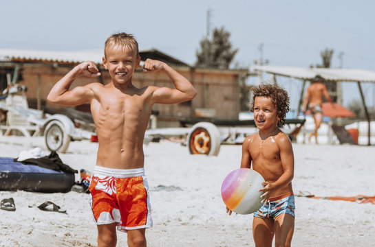funny curly-haired boy gymnast with a wide-toothed smile plays with his brother in blue water at sea on the beach on vacation