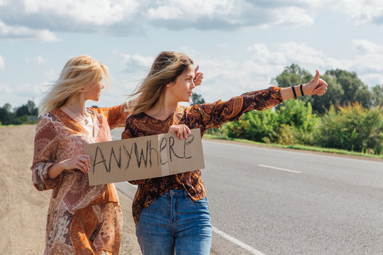 Two beautiful girls hitchhiking and vote with a sign ANYWHERE on road. Copy space.