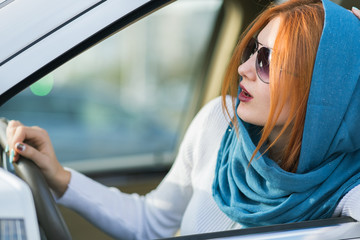 Young fashionable woman driver in scarf and sunglasses driving a car.