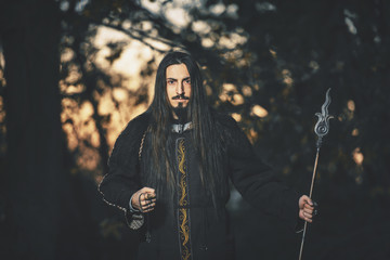 A man with long hair and beard in a black cloak in the image of a sorcerer warlock on Halloween....