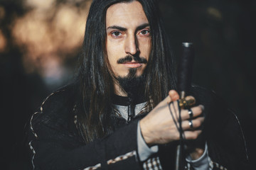 A man with long hair and beard in a black cloak in the image of a sorcerer warlock on Halloween....